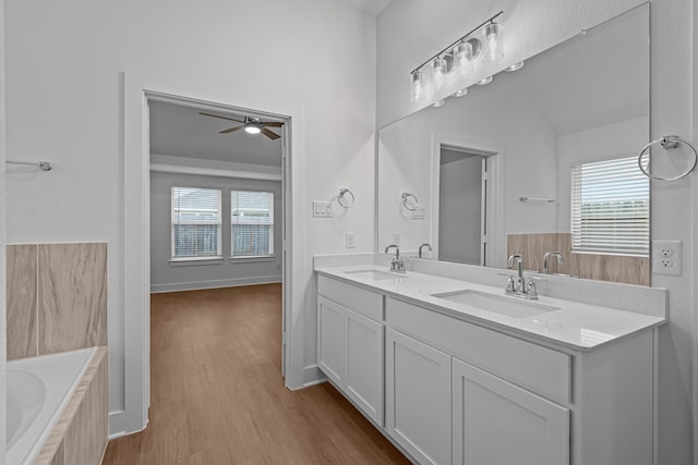 bathroom featuring wood-type flooring, a healthy amount of sunlight, a relaxing tiled tub, and vanity