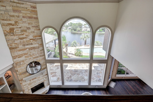 interior space with a water view, a towering ceiling, hardwood / wood-style flooring, and a fireplace