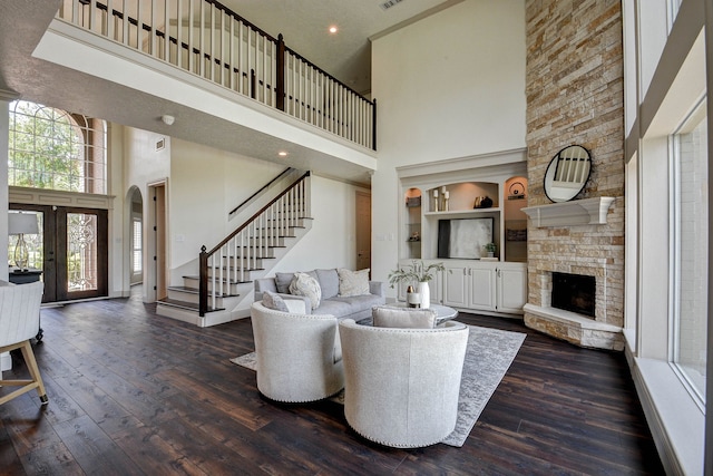 living room featuring built in features, a fireplace, dark hardwood / wood-style floors, and a towering ceiling