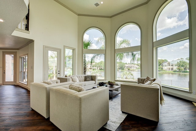 living room featuring ornamental molding, dark hardwood / wood-style flooring, a water view, and a high ceiling