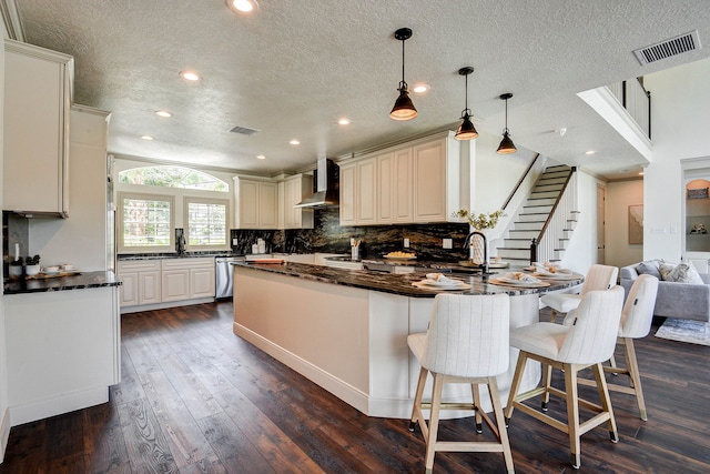 kitchen with a kitchen bar, dark wood-type flooring, wall chimney exhaust hood, and a textured ceiling