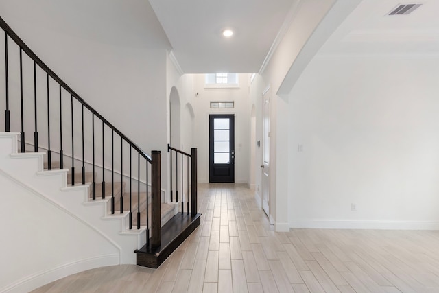 foyer with light hardwood / wood-style floors, crown molding, and a towering ceiling