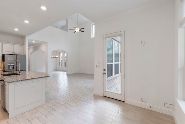 kitchen with light wood-type flooring, white cabinetry, light stone counters, sink, and ceiling fan