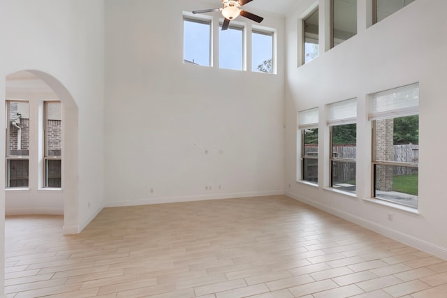 unfurnished living room with a healthy amount of sunlight, ceiling fan, a towering ceiling, and light hardwood / wood-style floors