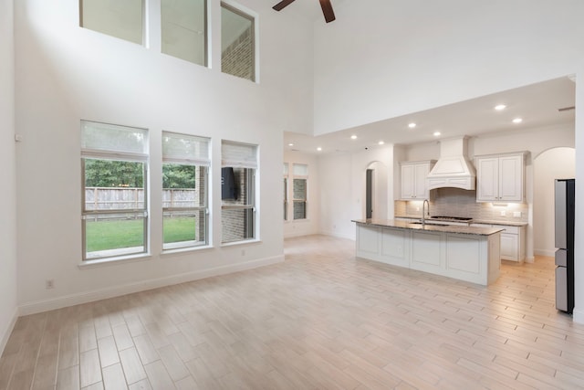 kitchen with light stone countertops, a center island with sink, light hardwood / wood-style flooring, ceiling fan, and custom exhaust hood