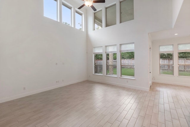 unfurnished living room featuring a high ceiling, ceiling fan, a wealth of natural light, and light hardwood / wood-style flooring