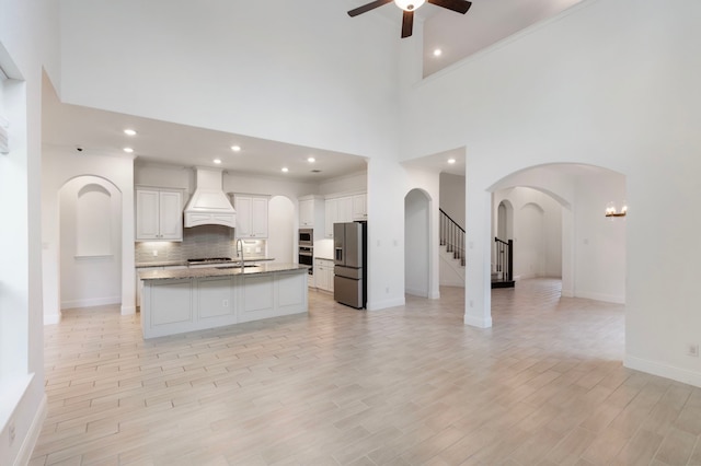 kitchen with light wood-type flooring, stainless steel appliances, premium range hood, ceiling fan, and white cabinets