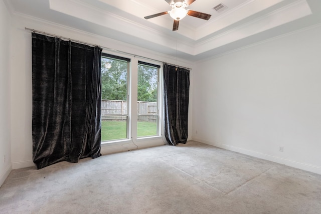 carpeted empty room featuring a healthy amount of sunlight, ceiling fan, ornamental molding, and a raised ceiling