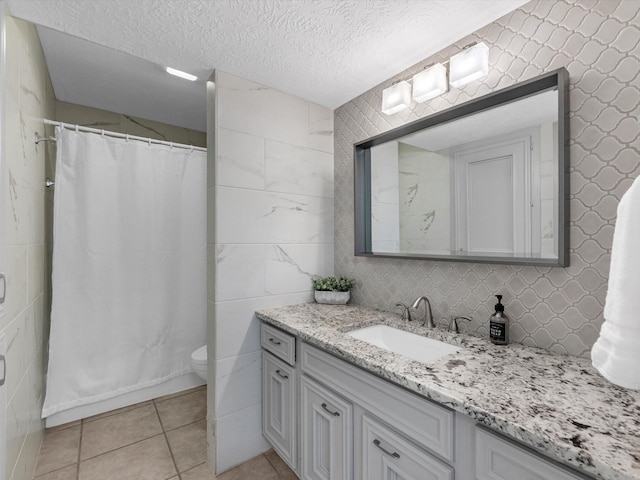 bathroom with a textured ceiling, vanity, tile patterned flooring, tile walls, and toilet