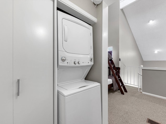 clothes washing area featuring light colored carpet, stacked washing maching and dryer, and a textured ceiling