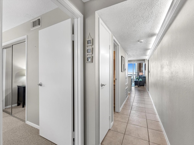 hall featuring light tile patterned floors, visible vents, a textured ceiling, and baseboards