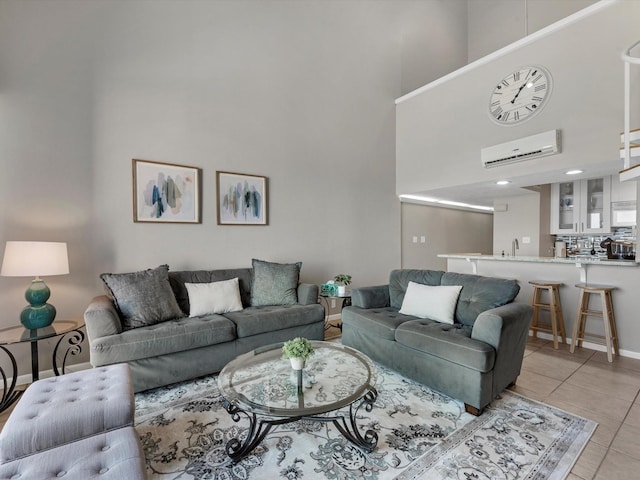 living room with light tile patterned floors, a towering ceiling, an AC wall unit, and baseboards