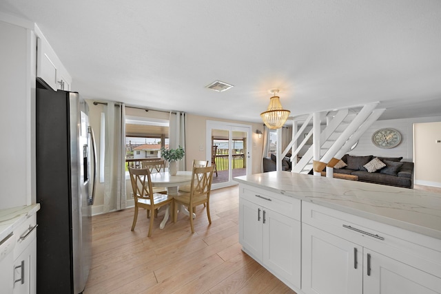 kitchen featuring light stone countertops, light hardwood / wood-style floors, white cabinetry, a chandelier, and stainless steel fridge