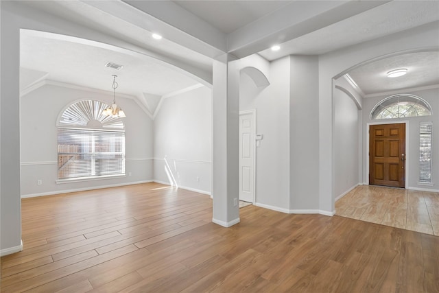 foyer with a notable chandelier, light wood-type flooring, crown molding, and vaulted ceiling