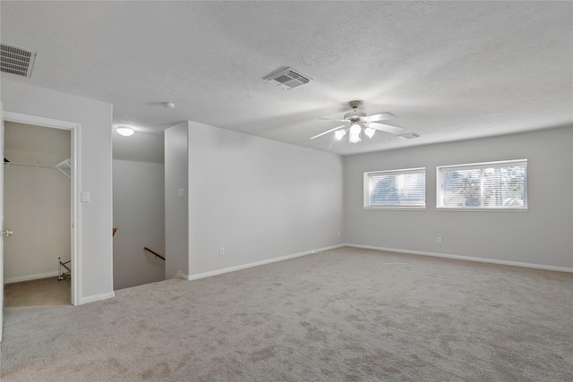 unfurnished room featuring ceiling fan, light colored carpet, and a textured ceiling