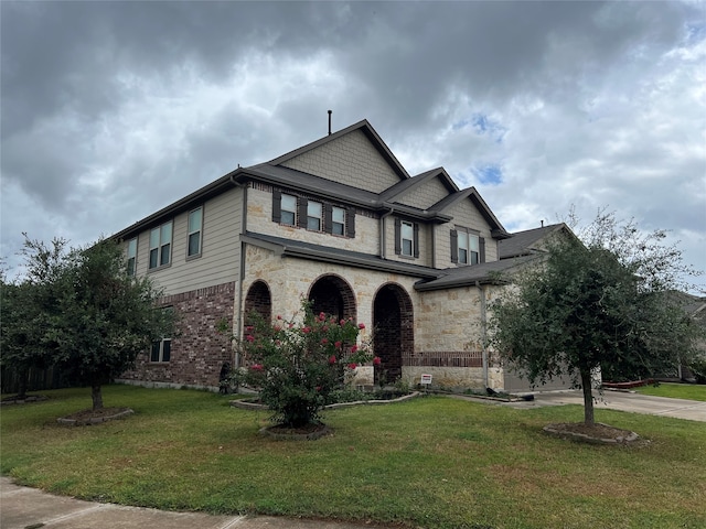 view of front of house featuring stone siding, a front lawn, concrete driveway, and brick siding