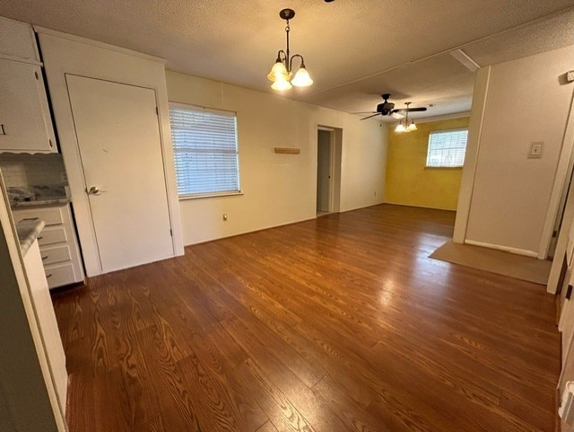 spare room with a textured ceiling, ceiling fan with notable chandelier, and dark hardwood / wood-style flooring