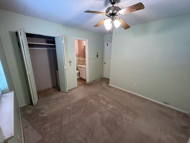 unfurnished bedroom featuring a closet, ensuite bathroom, ceiling fan, and carpet flooring