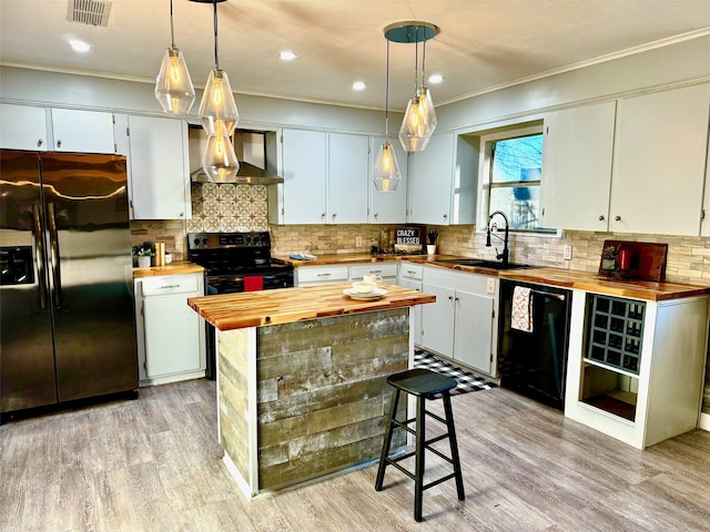 kitchen featuring wall chimney exhaust hood, black appliances, pendant lighting, ornamental molding, and butcher block counters