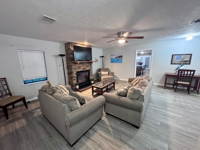 living room with ceiling fan, a fireplace, wood-type flooring, and a textured ceiling