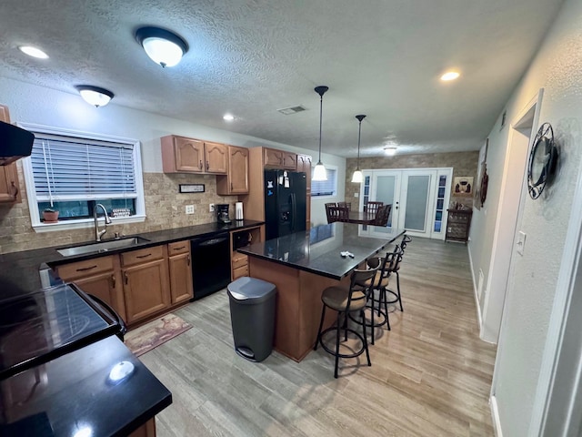 kitchen featuring black appliances, sink, light hardwood / wood-style floors, decorative light fixtures, and a kitchen island