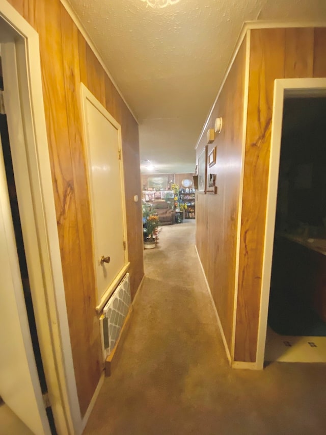 hall featuring a textured ceiling, wooden walls, and carpet floors