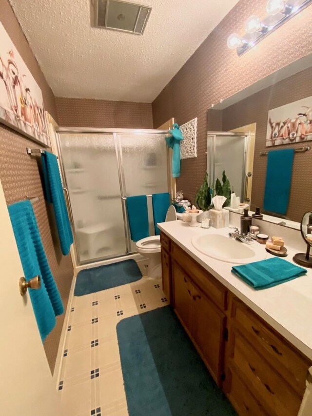 bathroom featuring vanity, toilet, a shower with shower door, and a textured ceiling