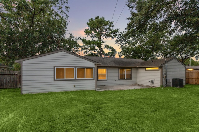 back house at dusk with central AC, a yard, and a patio