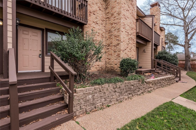 property entrance featuring a balcony, a chimney, fence, and brick siding