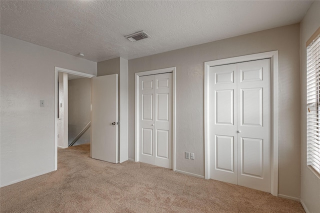 unfurnished bedroom featuring a textured ceiling, a textured wall, light carpet, visible vents, and two closets