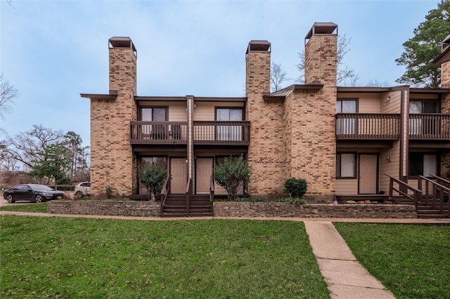 back of house with entry steps, a balcony, brick siding, a yard, and a chimney