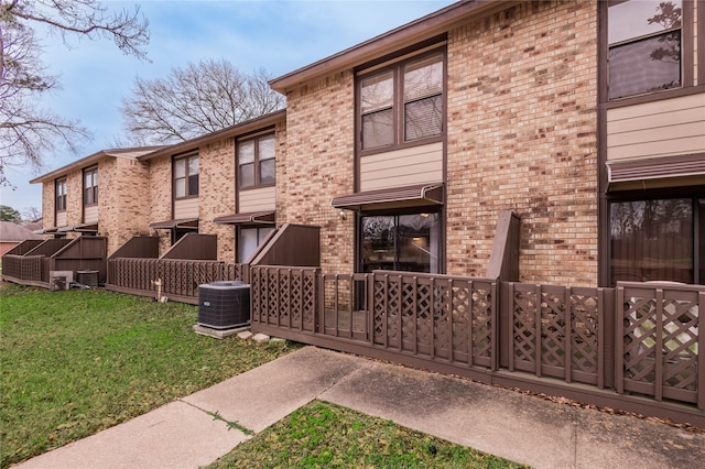 exterior space featuring central AC, a lawn, and brick siding