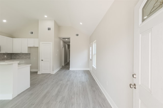 kitchen with high vaulted ceiling, backsplash, light wood-type flooring, and white cabinetry