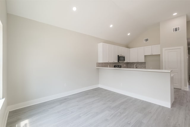 kitchen with white cabinets, light hardwood / wood-style flooring, kitchen peninsula, high vaulted ceiling, and tasteful backsplash