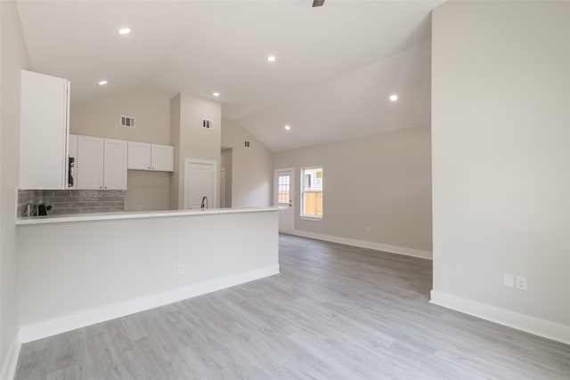 kitchen with high vaulted ceiling, white cabinetry, backsplash, sink, and light hardwood / wood-style floors