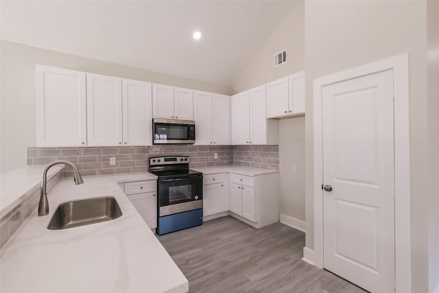 kitchen with appliances with stainless steel finishes, white cabinetry, light stone counters, and sink