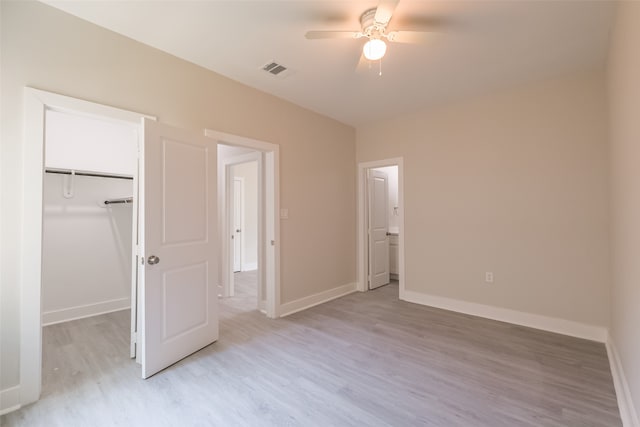 unfurnished bedroom featuring light wood-type flooring, a spacious closet, ceiling fan, and a closet