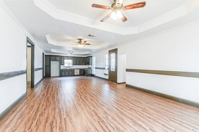 unfurnished living room with a tray ceiling, wood-type flooring, crown molding, and ceiling fan