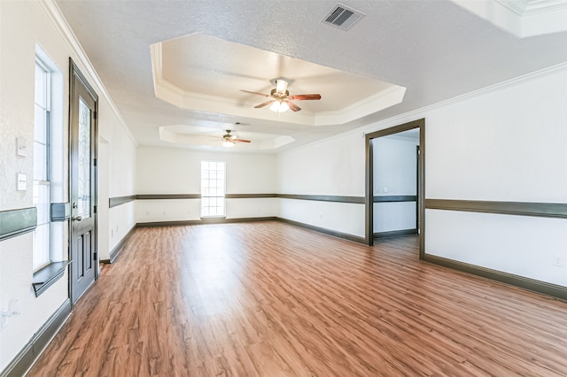 spare room with a textured ceiling, a tray ceiling, crown molding, hardwood / wood-style flooring, and ceiling fan