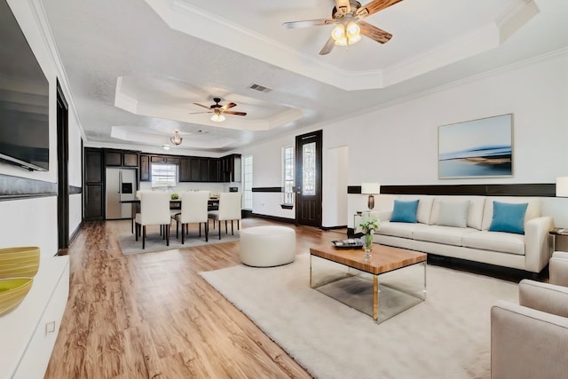 living room with plenty of natural light, a raised ceiling, ceiling fan, and light hardwood / wood-style flooring