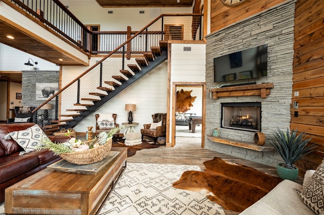 living room featuring wooden walls, a towering ceiling, light wood-type flooring, and a fireplace