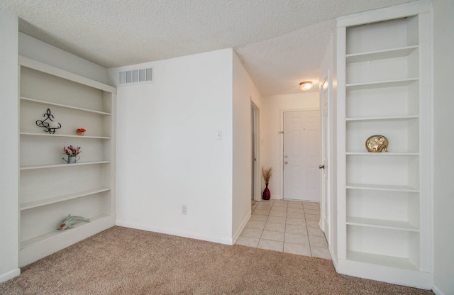 unfurnished room with built in shelves, light colored carpet, and a textured ceiling