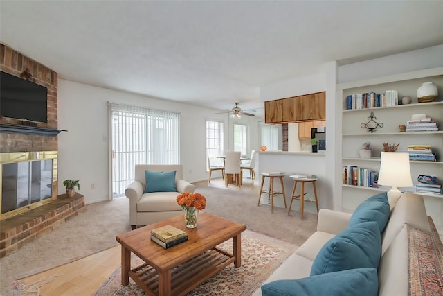 living room with built in shelves, ceiling fan, light carpet, and a fireplace