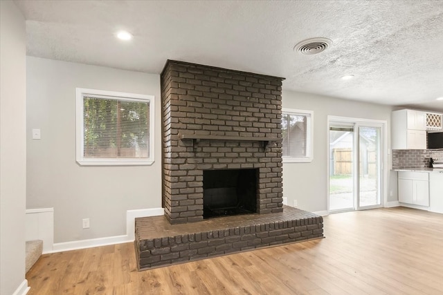 unfurnished living room featuring a fireplace, a textured ceiling, and light hardwood / wood-style floors