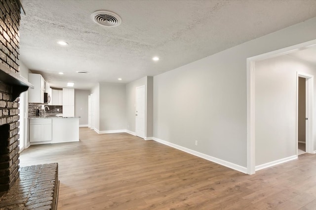 unfurnished living room with a textured ceiling, sink, light wood-type flooring, and a brick fireplace