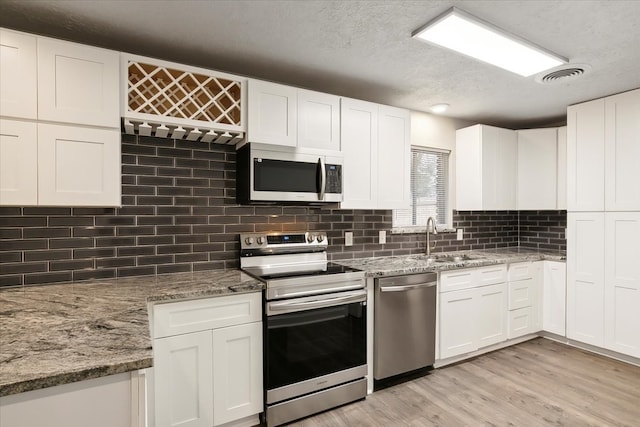 kitchen featuring white cabinetry, backsplash, sink, appliances with stainless steel finishes, and light hardwood / wood-style floors