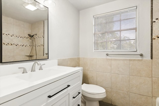 bathroom with tiled shower, vanity, toilet, and tile walls