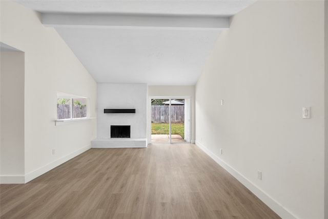 unfurnished living room with a wealth of natural light, a fireplace, light hardwood / wood-style floors, and vaulted ceiling with beams