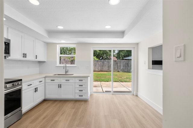 kitchen with appliances with stainless steel finishes, light hardwood / wood-style floors, white cabinetry, sink, and tasteful backsplash