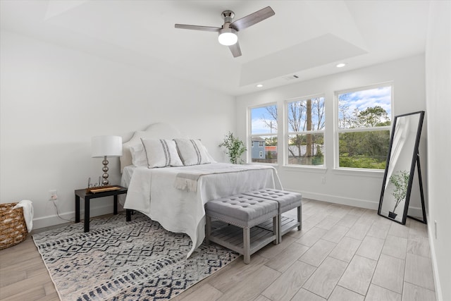 bedroom with ceiling fan, a tray ceiling, and light hardwood / wood-style flooring